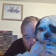 Max is registered to the contest to win money with this photo: person, dog, indoor, cd_collection, shelf, portrait, pet, furniture, wall_art, collar, face, beard, hair, table, bottle, door, room, casual, holding, closeup