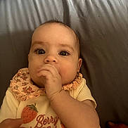Brynlee is registered to the contest to win money with this photo: baby, child, infant, portrait, face, eyes, hand, fist, sitting, lying_down, bed, bedding, blanket, bib, floral, clothing, strawberry, indoors, cozy, curious