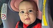 Brynlee joined the competition — help win amazing prizes! baby, child, infant, car_seat, harness, portrait, face, eyes, wide_eyed, sitting, red_shirt, black_clothing, pink_padding, vehicle, interior, safety, close_up, looking_at_camera, alert, photograph