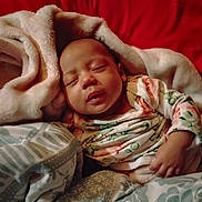 Jayla is registered to the contest to win money with this photo: baby, blanket, child, comfort, cozy, cute, floral_onesie, hand, head, indoors, infant, peaceful, portrait, red_background, relaxed, resting, sleeping, sleepwear, soft_texture, young