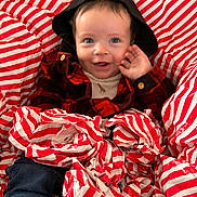 Denver is registered to the contest to win money with this photo: baby, child, smiling, hood, plaid_shirt, wrapping_paper, red_and_white, blue_eyes, waving_hand, sitting, clothing, cute, indoor, happy, portrait, infant, festive, cozy, casual, cheerful
