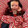 baby, child, smiling, hood, plaid_shirt, wrapping_paper, red_and_white, blue_eyes, waving_hand, sitting, clothing, cute, indoor, happy, portrait, infant, festive, cozy, casual, cheerful