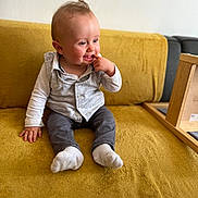 Mylan a rejoint le concours — aidez-le/la à gagner de superbes lots ! baby, child, sitting, couch, yellow_couch, clothing, socks, vest, long_sleeve_shirt, indoor, furniture, person, cute, infant, portrait, hand, face, expression, curious, wooden_frame