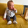 baby, child, sitting, couch, yellow_couch, clothing, socks, vest, long_sleeve_shirt, indoor, furniture, person, cute, infant, portrait, hand, face, expression, curious, wooden_frame