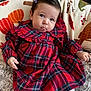 baby, child, plaid_dress, red_clothing, blanket, autumn_theme, pumpkin_pattern, cozy, cute, tongue_out, hair_clip, indoor, seated, smiling, infant, soft_texture, person, portrait, young_child, warm_colors