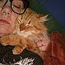 blanket, cat, close_up, comfort, cozy, eyewear, face, fur, glasses, hand, indoor, nose_ring, orange_cat, person, pet, relaxation, resting, sleeping, snuggling, tshirt