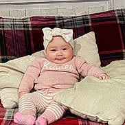 Cielo is registered to the contest to win money with this photo: baby, infant, child, bow_headband, pink_sweater, striped_pants, socks, plaid_blanket, couch, pillow, cozy, smile, cheeks, seated, indoors, textile, portrait, home, furniture, cute