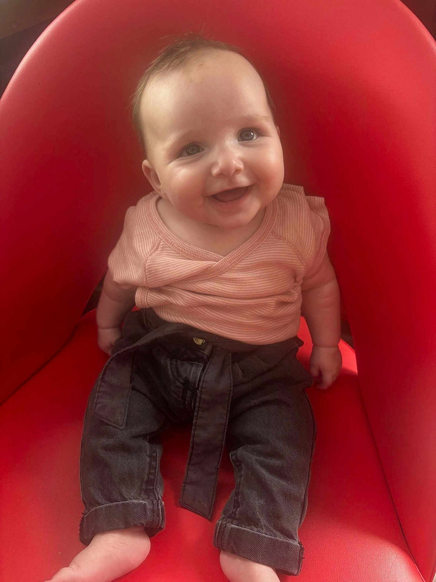 éléna participe au concours pour gagner de l'argent avec cette photo : baby, child, smiling, red_chair, pink_shirt, dark_pants, barefoot, sitting, cute, happy, indoor, face, person, infant, portrait, clothing, furniture, young_child, bright_color, casual_wear