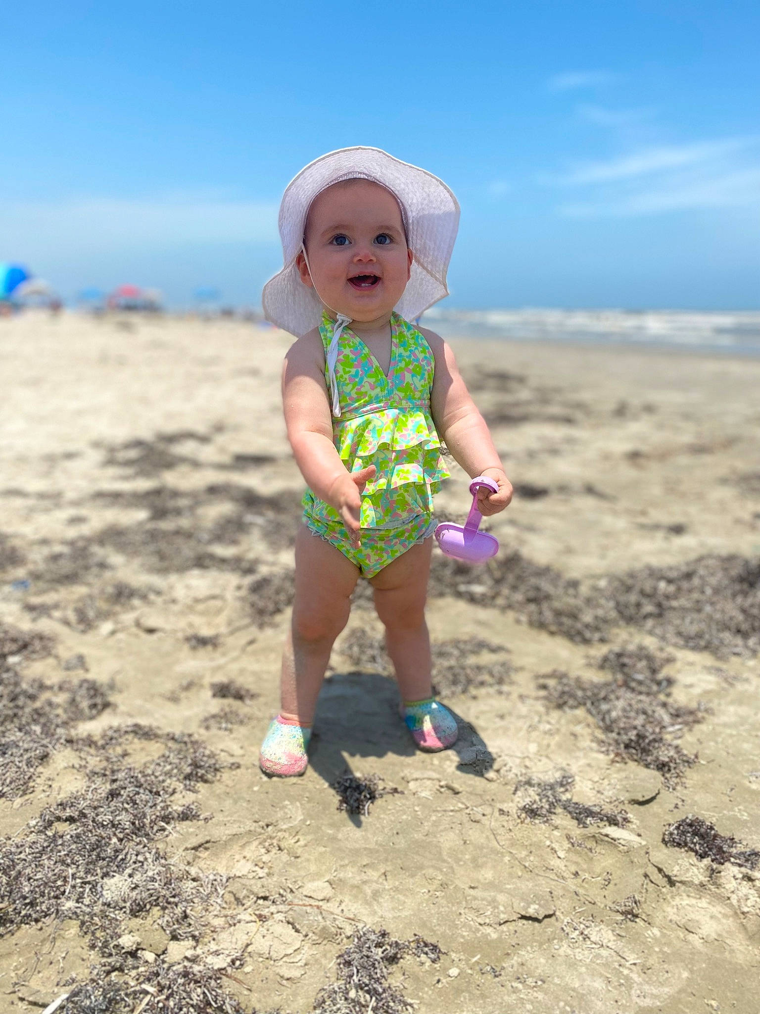 Leighton is registered to the contest to win money with this photo: beach, body_of_water, cloud, coast, fun, happy, hat, horizon, landscape, leisure, people_in_nature, people_on_beach, person, recreation, sand, shore, sky, sun_hat, t_shirt, toddler