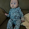 animal_print, baby, blanket, child, comfortable, couch, cozy, curious, cute, furniture, home, indoor, infant, onesie, person, plush, portrait, seated, soft_lighting, wide_eyes