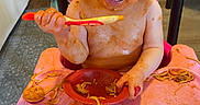 November is registered to the contest to win money with this photo: toddler, messy, spaghetti, sauce, food, high_chair, pink, smiling, happy, baby, indoor, feeding, child, plate, utensil, hair, face, hands, kitchen, eating