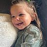 toddler, child, smiling, happy, baby_yoda, sweater, green_bow, hair_accessory, couch, pillow, plush, cozy, indoor, cute, portrait, childhood, relaxing, casual_clothing, home, snuggling