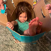 Mötley joined the competition — help win amazing prizes! child, cardboard_box, playful, indoor, carpet, toy, hands, feet, smiling, girl, green_dress, hair, cozy, fun, family, home, cute, young, person, relaxed