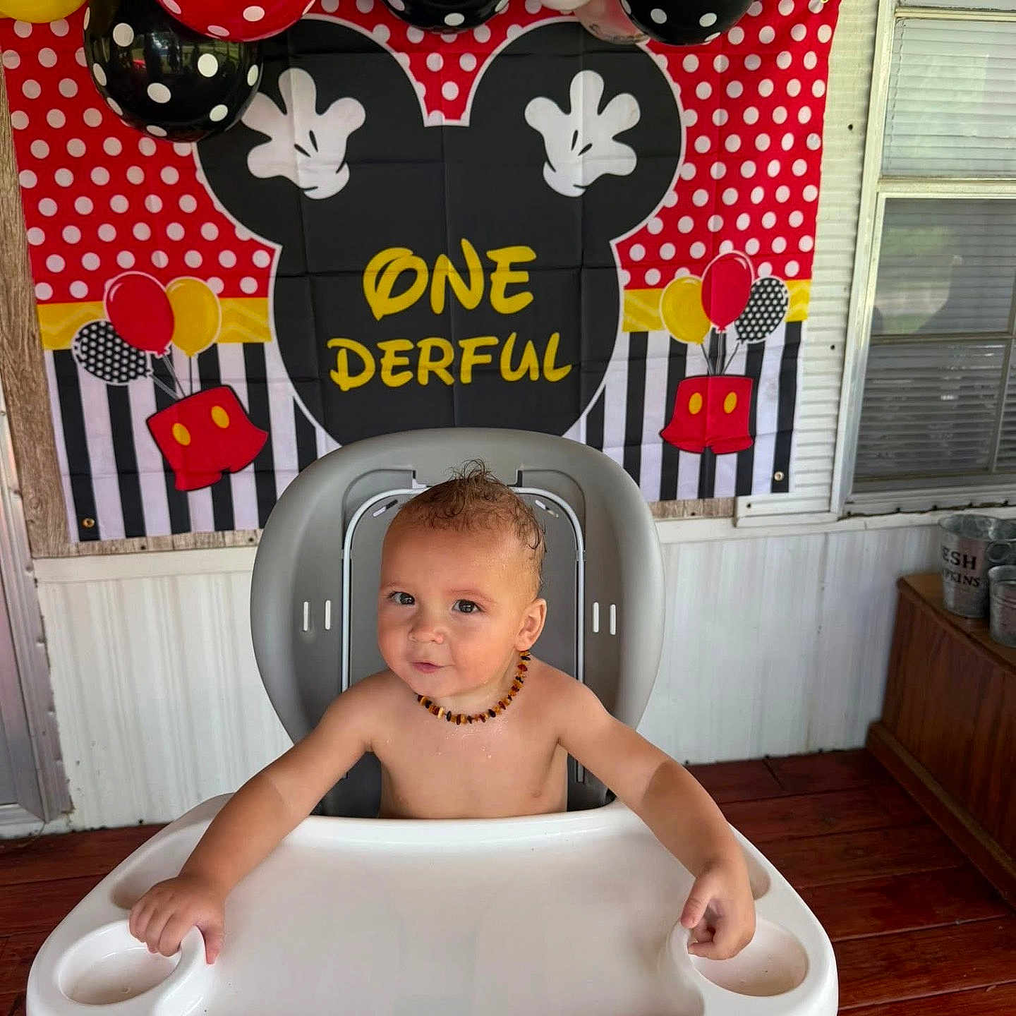 Zachery is registered to the contest to win money with this photo: baby, high_chair, balloons, birthday, mickey_mouse, polka_dots, child, smiling, party, celebration, indoor, decorations, necklace, cute, toddler, face, expression, red, yellow, black