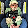 baby, infant, car_seat, pacifier, clothing, green_hat, mittens, footwear, blue_cushion, seatbelt, safety_harness, newborn, cute, indoors, portrait, expression, tiny_feet, fabric, warning_label, child