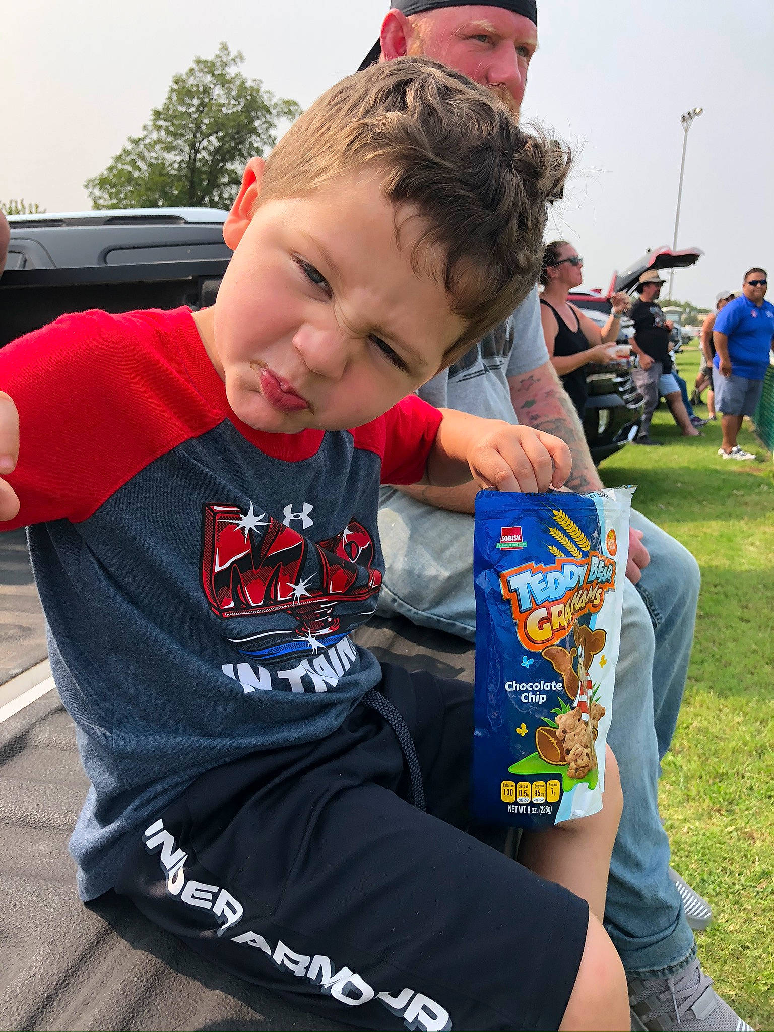 King joined the competition — help win amazing prizes! baseball_cap, cap, child, competition_event, event, fun, grass, hairstyle, headwear, leisure, person, public_event, recreation, sitting, sky, sleeve, t_shirt, team, toddler, tree