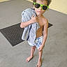 Ja'Kobe Anthony is registered to the contest to win money with this photo: child, boy, sunglasses, towel, barefoot, shorts, curly_hair, indoor, concrete_floor, mat, yellow_wall, portrait, standing, casual, summer, cool, person, fashion, expressionless, young