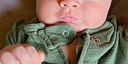 Ezra is registered to the contest to win money with this photo: baby, infant, face, blue_eyes, green_clothing, zipper, hand, skin, cute, portrait, newborn, child, lying_down, expression, fist, soft_texture, indoors, person, young_child, closeup