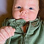 baby, infant, face, blue_eyes, green_clothing, zipper, hand, skin, cute, portrait, newborn, child, lying_down, expression, fist, soft_texture, indoors, person, young_child, closeup