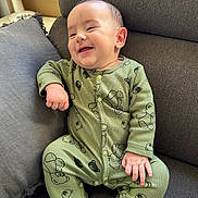 Gabriel a rejoint le concours — aidez-le/la à gagner de superbes lots ! baby, smiling, green_onesie, teddy_bear_print, couch, grey_cushion, infant, happy, indoor, child, cute, sitting, portrait, face, hand, footwear_infant, cozy, home, relaxing, fan