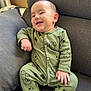baby, smiling, green_onesie, teddy_bear_print, couch, grey_cushion, infant, happy, indoor, child, cute, sitting, portrait, face, hand, footwear_infant, cozy, home, relaxing, fan
