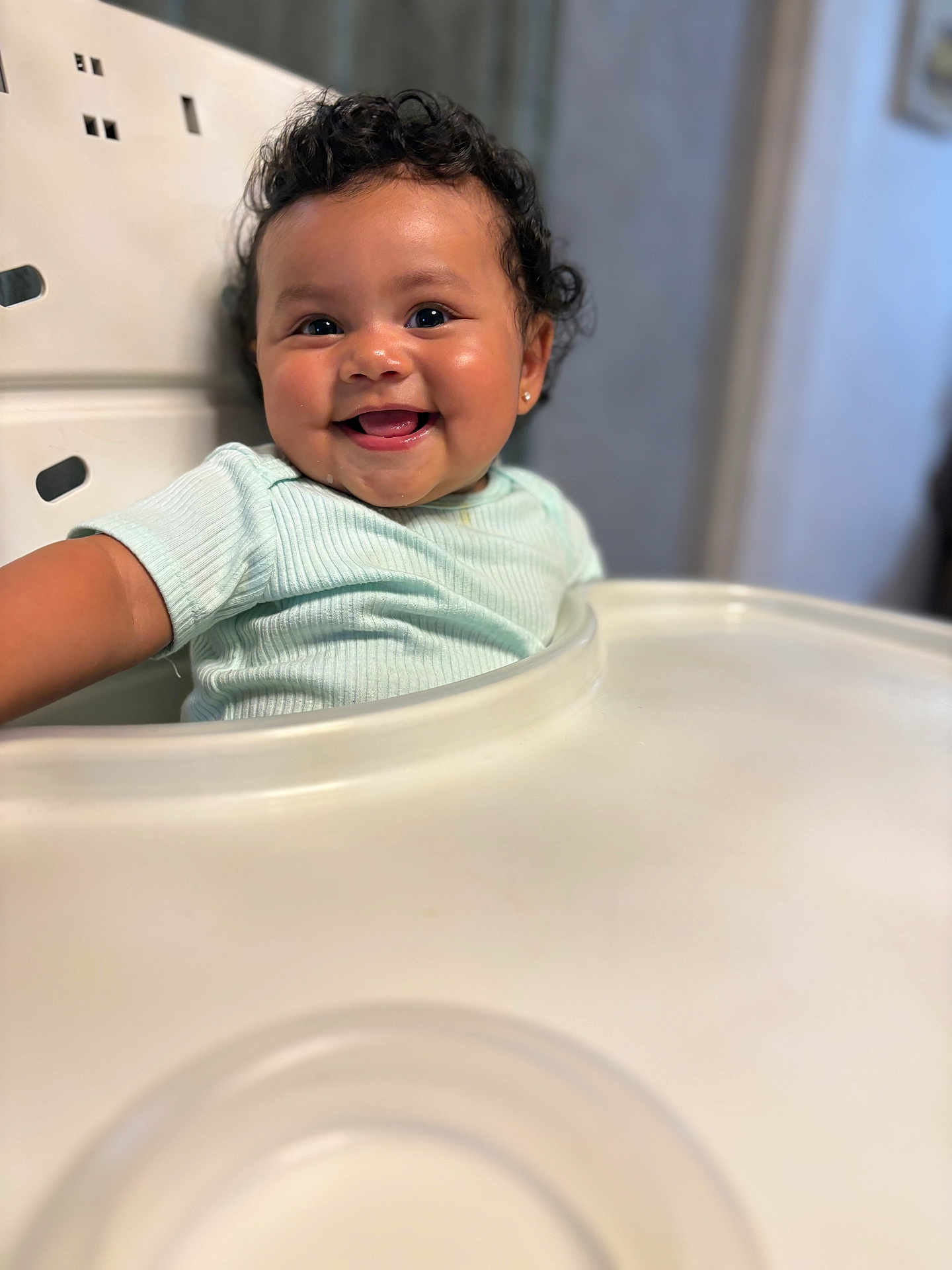 Victoria joined the competition — help win amazing prizes! baby, child, smile, curly_hair, high_chair, happy, indoor, person, cute, infant, sitting, clothing, face, earrings, tongue, table, skin, young, portrait, bright