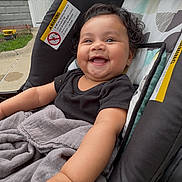 Victoria joined the competition — help win amazing prizes! baby, smiling, stroller, blanket, outdoor, curly_hair, happy, child, person, black_shirt, hand, face, suburban, door, sidewalk, grass, toy, earrings, fabric, window