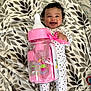 baby, smiling, blanket, leaf_pattern, onesie, polka_dots, toy, pink, bottle, cute, infant, happy, lying_down, face, child, comfort, playful, room, soft, accessory