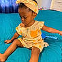 Nevaeh is registered to the contest to win money with this photo: toddler, child, bed, blue_bedspread, curly_hair, headband, romper, orange_prints, sitting, indoor, furniture, person, clothing, earrings, cute, expression, skin, hair, room, window_curtain