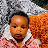 Janiyah is registered to the contest to win money with this photo: baby, infant, child, pink_clothing, floral_pattern, white_collar, couch, pillow, orange_pillow, indoor, portrait, face, curly_hair, cute, seated, looking_at_camera, soft_lighting, home, cozy, young_child