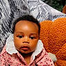 baby, infant, child, pink_clothing, floral_pattern, white_collar, couch, pillow, orange_pillow, indoor, portrait, face, curly_hair, cute, seated, looking_at_camera, soft_lighting, home, cozy, young_child