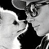 Chanel participe au concours pour gagner de l'argent avec cette photo : dog, person, portrait, black_and_white, fluffy, white_dog, face, nose_to_nose, glasses, cap, close_up, profile, animal, pet, companionship, affection, dramatic_lighting, dark_background, photography, outdoor