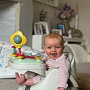 Brea is registered to the contest to win money with this photo: baby, infant, smile, tongue_out, striped_clothing, baby_seat, toy, play, happy, child, indoor, carpet, foot, hand, face, person, living_room, furniture, decor, photography