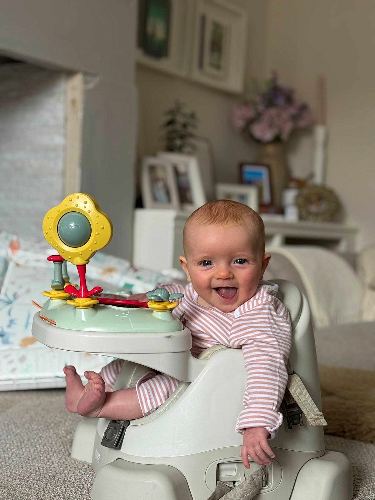Brea is registered to the contest to win money with this photo: baby, infant, smile, tongue_out, striped_clothing, baby_seat, toy, play, happy, child, indoor, carpet, foot, hand, face, person, living_room, furniture, decor, photography