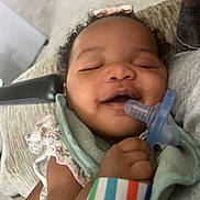 Cimani joined the competition — help win amazing prizes! baby, infant, pacifier, smile, curly_hair, blanket, arm, wristband, clothing, closeup, resting, happy, skin, person, indoor, comfort, holding, peaceful, cute, portrait