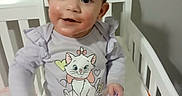Delanie joined the competition — help win amazing prizes! baby, child, crib, purple_bow, cartoon_cat, shirt, white_pants, socks, indoor, happy, smiling, hand, face, hair, person, furniture, bed, cute, infant, home
