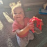 toddler, child, toy, red_toy, carpet, sunlight, indoor, pigtails, smiling, kneeling, playtime, happy, cute, casual_clothing, home, person, young_child, bright, shadow, fun