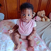 Braylen joined the competition — help win amazing prizes! baby, infant, child, pink_bib, blanket, stuffed_animal, teddy_bear, wood_paneling, bed, curly_hair, wide_eyes, sitting, indoors, cute, portrait, clothing, soft_toys, furniture, skin, person