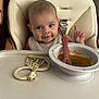 baby, bib, child, cute, expression, face, feeding, food, giraffe_toy, high_chair, indoor, infant, messy, person, seat, smile, spoon, table, teething_toy, tray