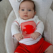 Matéo a rejoint le concours — aidez-le/la à gagner de superbes lots ! baby, infant, child, face, blue_eyes, white_shirt, red_shorts, fish_graphic, cushioned_seat, plush_toy, soft_fabric, indoor, portrait, cute, small_hands, sitting, curious, young, clothing, person