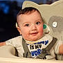 baby, child, high_chair, smile, face, eyes, shirt, strap, rosy_cheeks, indoor, seated, happy, cute, infant, person, portrait, closeup, childhood, babywear, feeding_chair