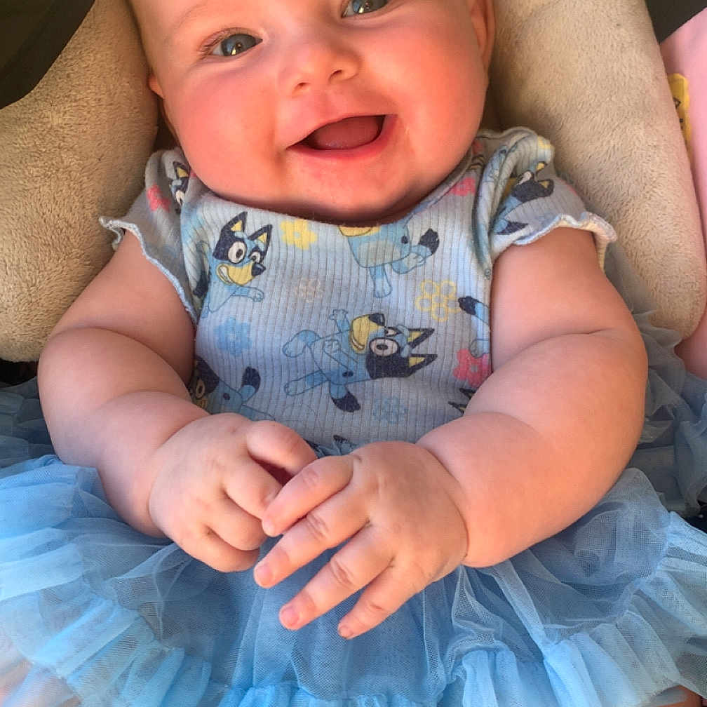 Lillianna is registered to the contest to win money with this photo: baby, blue_dress, cheerful, child, chubby_arms, clothing, cute, eyes, face, hands, happy, indoors, infant, padded_seat, portrait, seat, sitting, skin, smiling, tutu