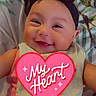 baby, smiling, headband, bow, bib, pink_clothing, blanket, indoor, portrait, child, cute, happy, infant, face, person, sitting, text_overlay, heart, accessory, closeup