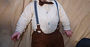 Wesson James joined the competition — help win amazing prizes! baby, infant, suspenders, bow_tie, clothing, blanket, bed, person, child, cute, expression, face, hands, feet, indoors, fabric, portrait, laying_down, curious, human