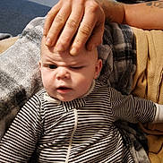 Wesson James is registered to the contest to win money with this photo: baby, child, striped_clothing, hand, adult_hand, facial_expression, confused, blanket, couch, indoor, person, portrait, toddler, skin, head, face, sitting, comfort, home, cozy