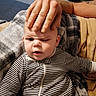 baby, child, striped_clothing, hand, adult_hand, facial_expression, confused, blanket, couch, indoor, person, portrait, toddler, skin, head, face, sitting, comfort, home, cozy