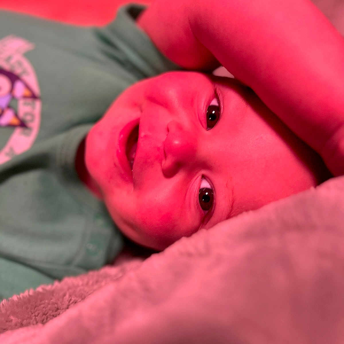 Wesson James joined the competition — help win amazing prizes! baby, child, smiling, face, arm, blanket, green_shirt, close_up, happy, portrait, infant, soft_texture, indoor, cute, lying_down, expression, skin, person, toddler, colorful