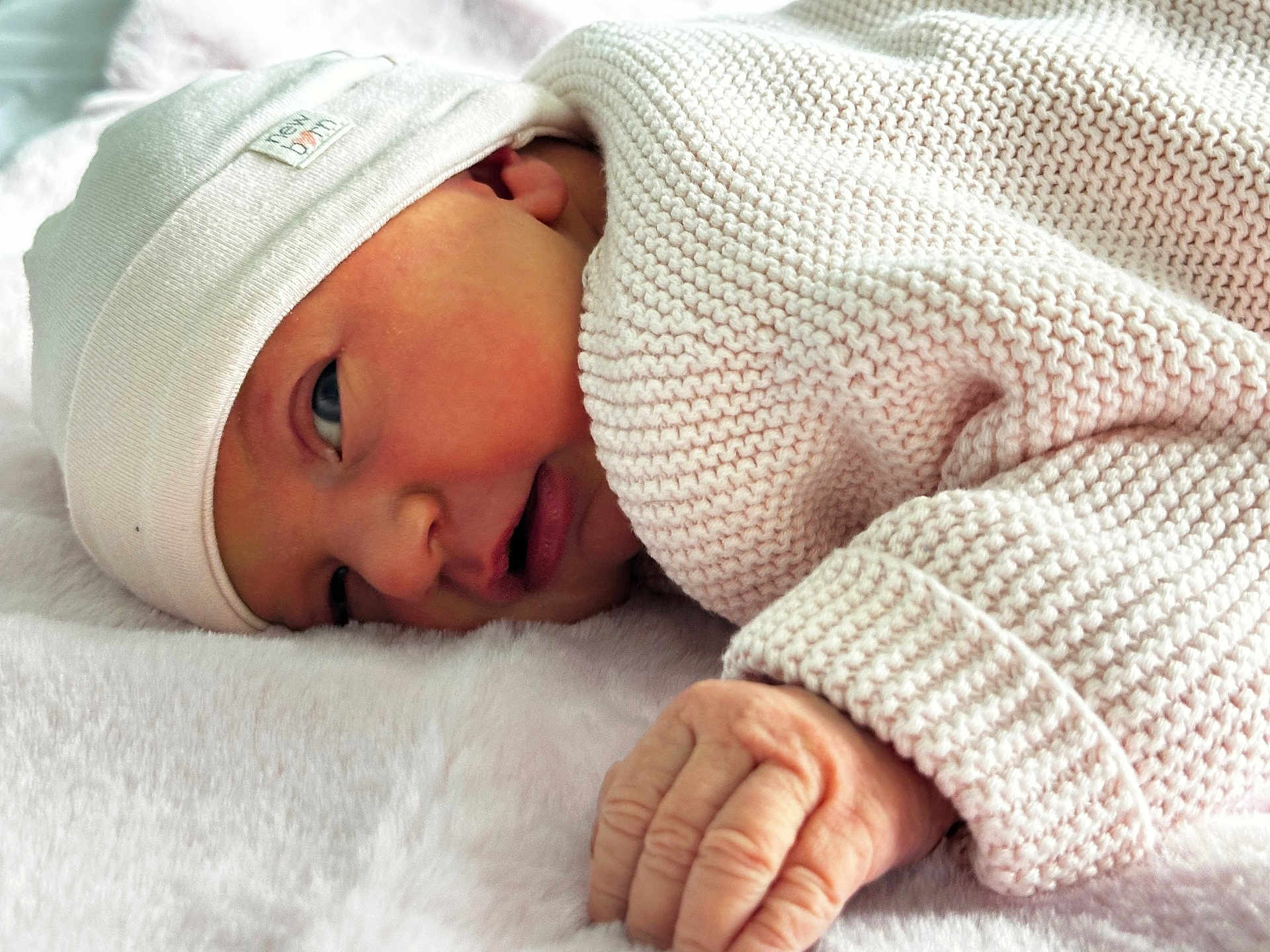 Elise participe au concours pour gagner de l'argent avec cette photo : newborn, baby, infant, knitted_clothing, white_cap, lying_down, fluffy_blanket, close_up, hand, skin, face, sleepy, cute, soft_texture, warm, resting, portrait, cozy, child, baby_clothes