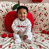baby, child, smiling, sitting, plush_toy, cherry_pattern, decorations, indoor, cute, white_clothing, face, portrait, soft_toys, background, home_decor, infant, happy, playful, cozy, colorful