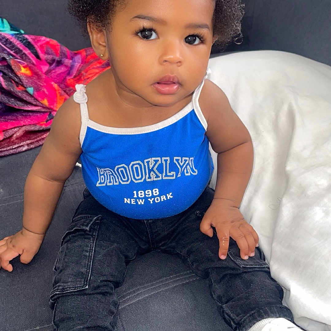 Loëlya a rejoint le concours — aidez-le/la à gagner de superbes lots ! toddler, child, baby, blue_bow, blue_tank_top, brooklyn, sitting, couch, blanket, curly_hair, white_shoes, casual_clothing, indoor, portrait, cute, small_hands, expressive_eyes, fashion, comfortable, colorful